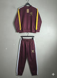 Maroon tracksuit with yellow and white accents on hangers against a gray background